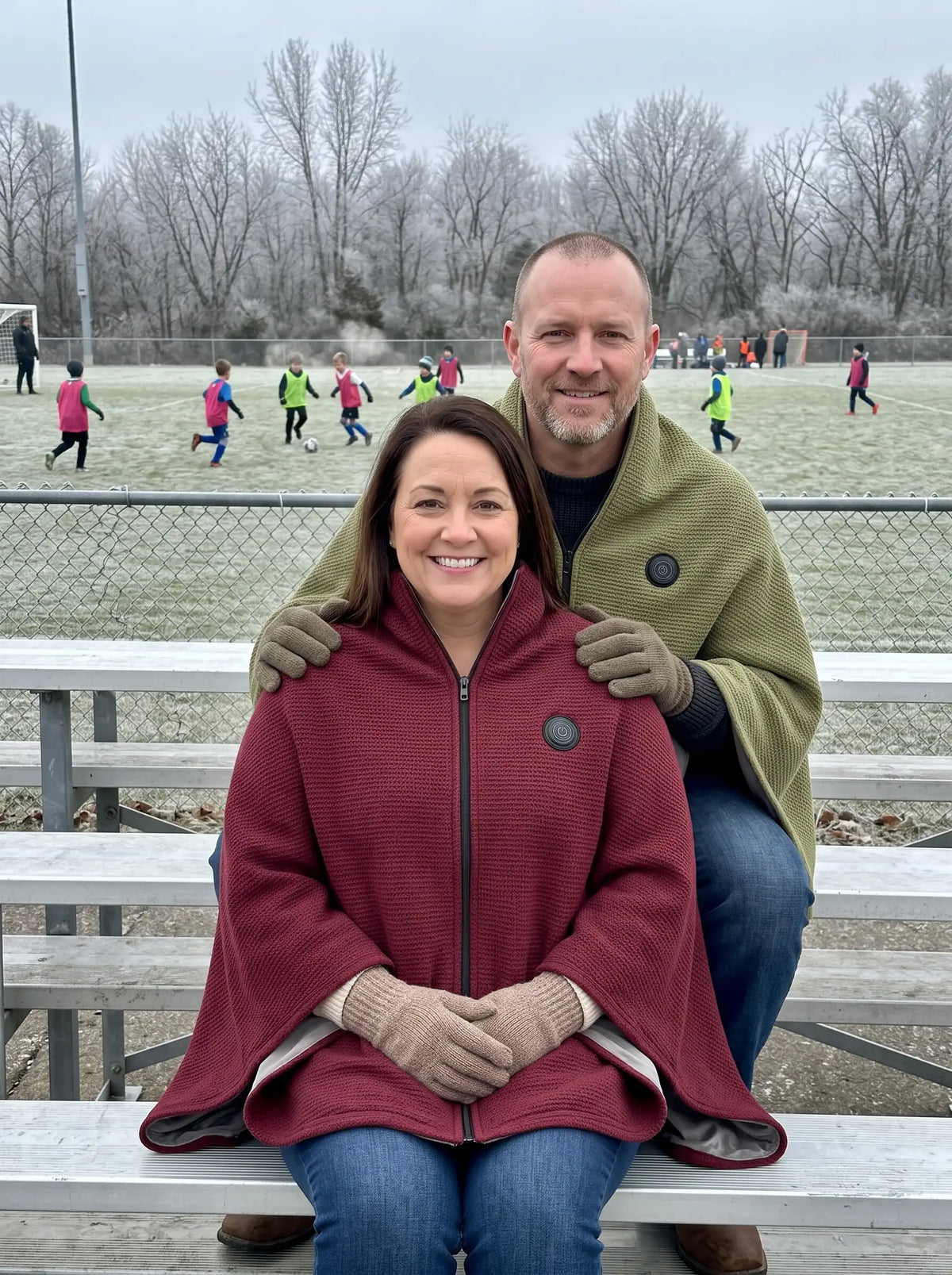 Parents watching a kids game in the cold, both wearing the AerPack WarmWrap