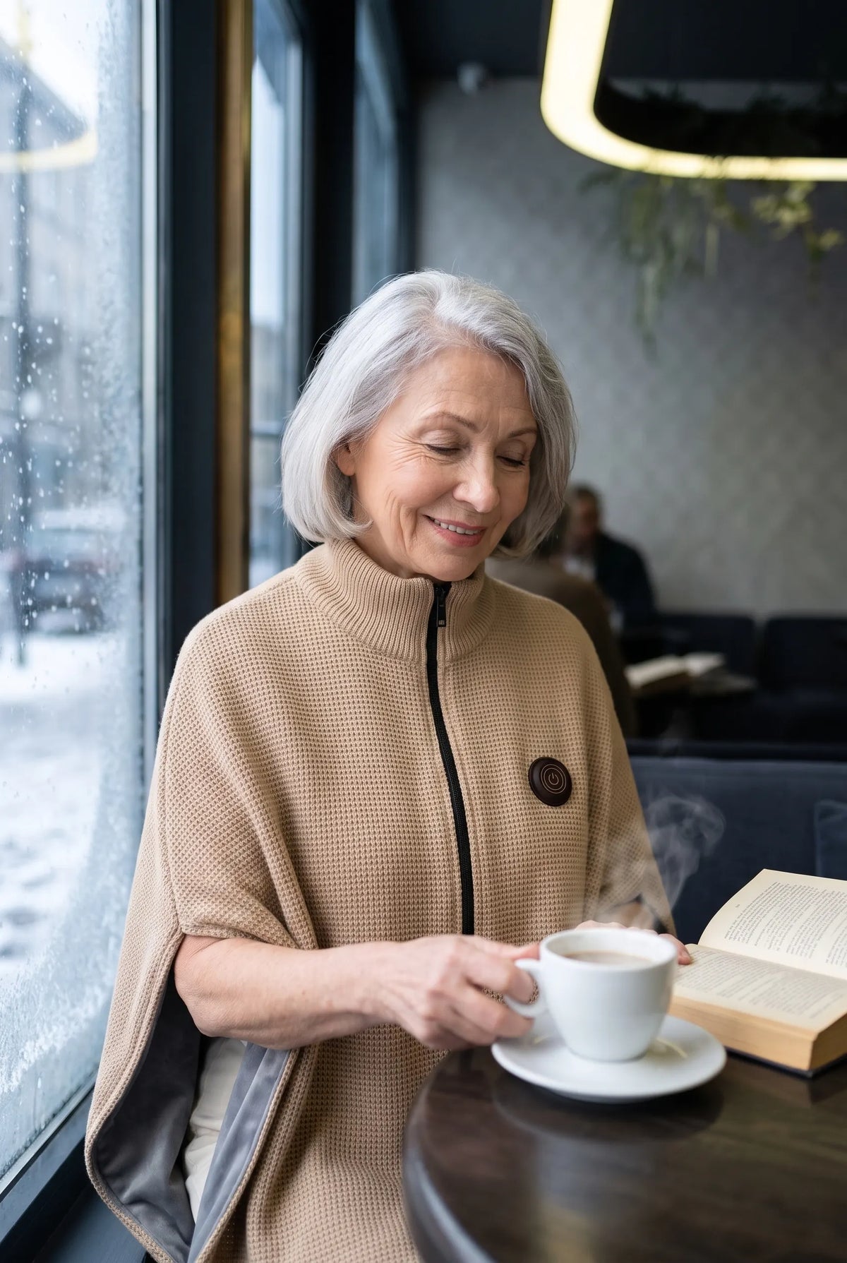 Woman with a steaming coffee by a frosted window in the beige AerPack WarmWrap